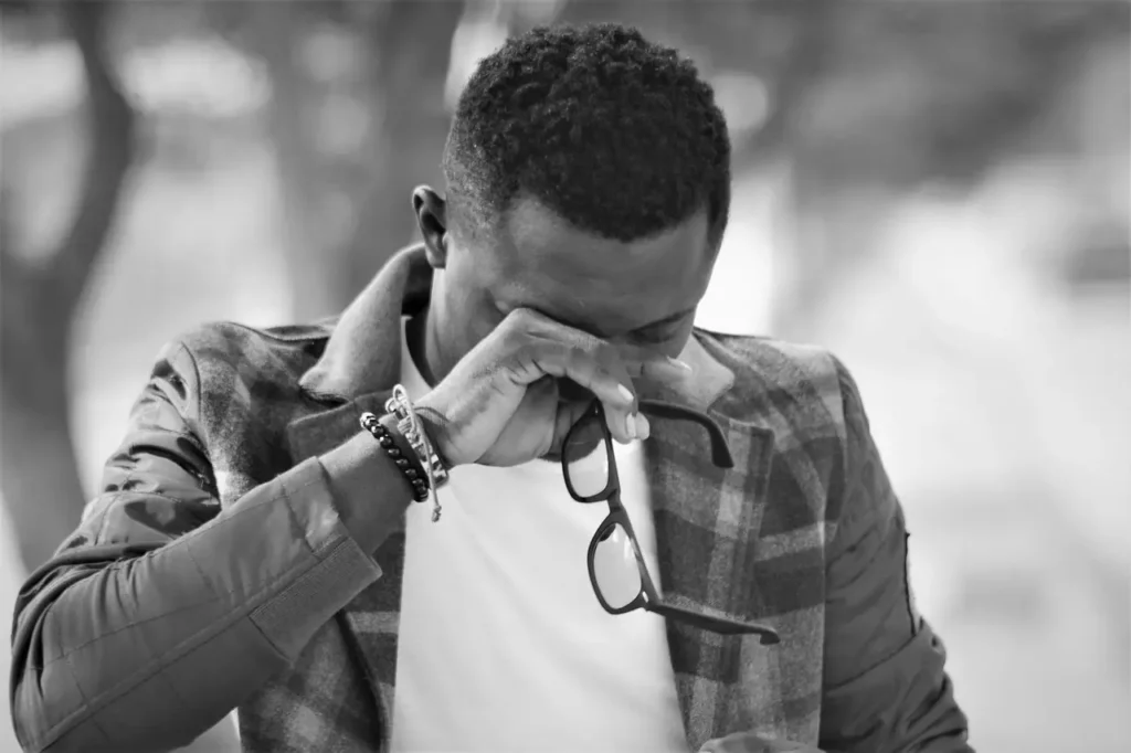 An African Man holding his glasses and crying