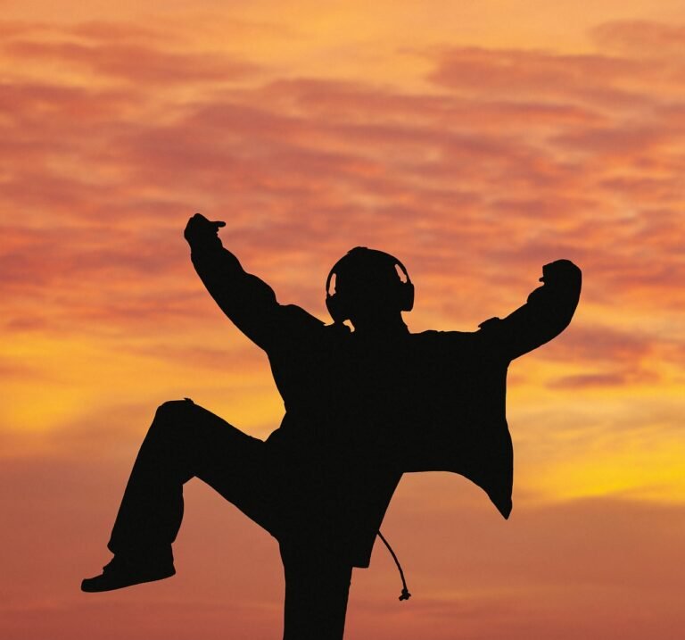 Silhouette of a man with headphones celebrating at sunrise, symbolizing reconnection to his body and life force