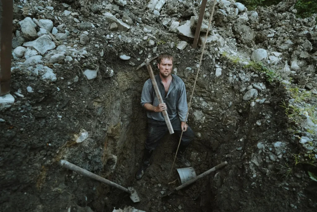 Man standing in a deep trench holding a pickaxe, symbolizing inner excavation and masculine identity